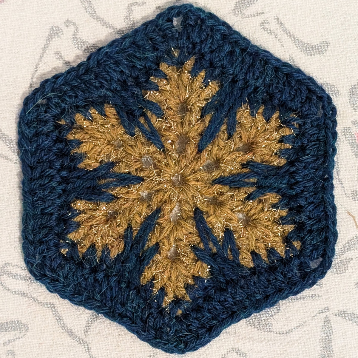 Crocheted square with a gold snowflake design on a textured background