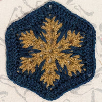 Crocheted square with a gold snowflake design on a textured background