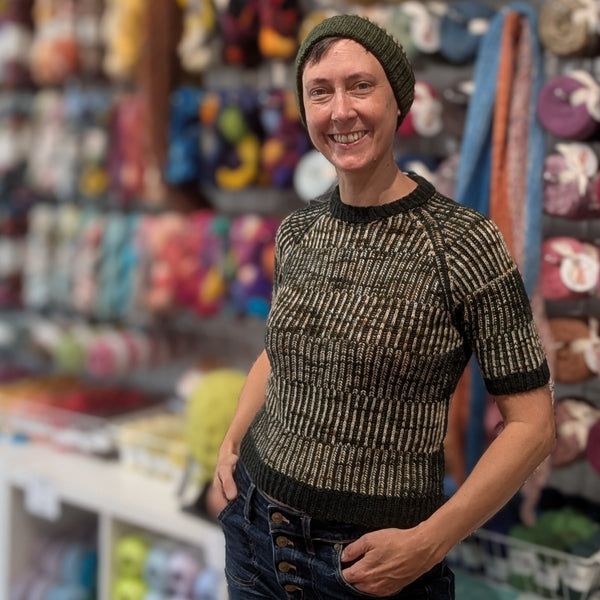 Person wearing a patterned sweater and green beanie in a store with colorful items on shelves.