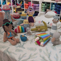 Collection of colorful crochet toys on a table with yarn shelves in the background