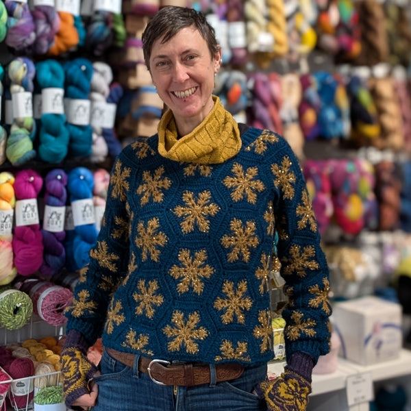 Person wearing a blue sweater with yellow snowflake patterns in a yarn store.
