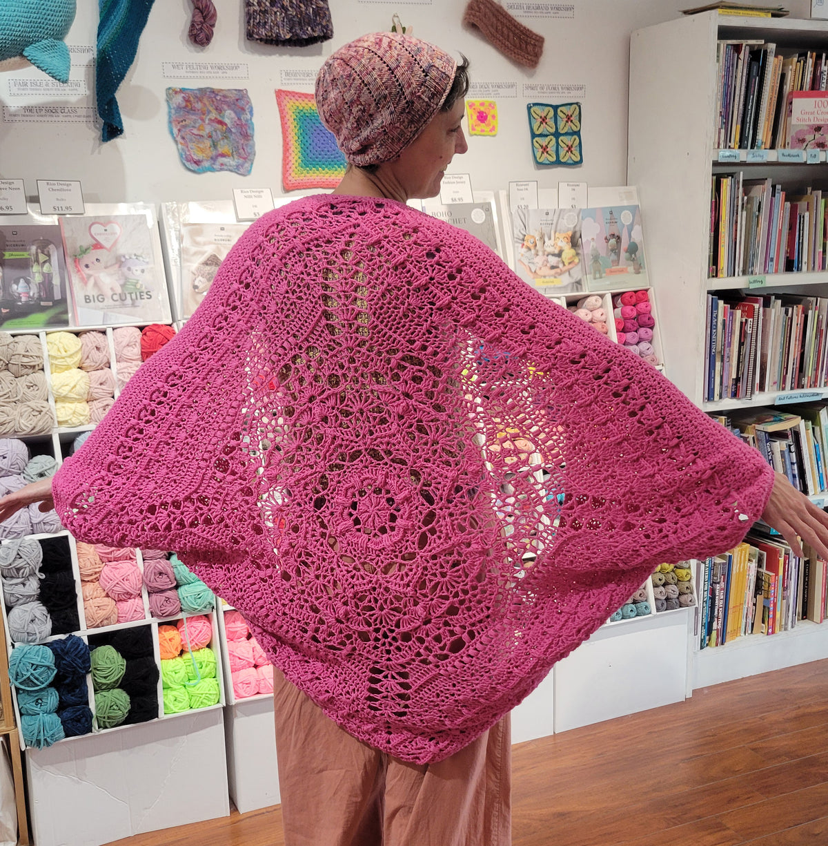 Person wearing a pink crocheted shawl in a yarn store