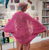 Person wearing a pink crocheted shawl in a yarn store