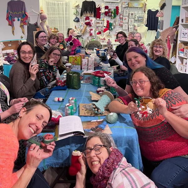 A group of people smiling and working on various craft projects at a holiday party.